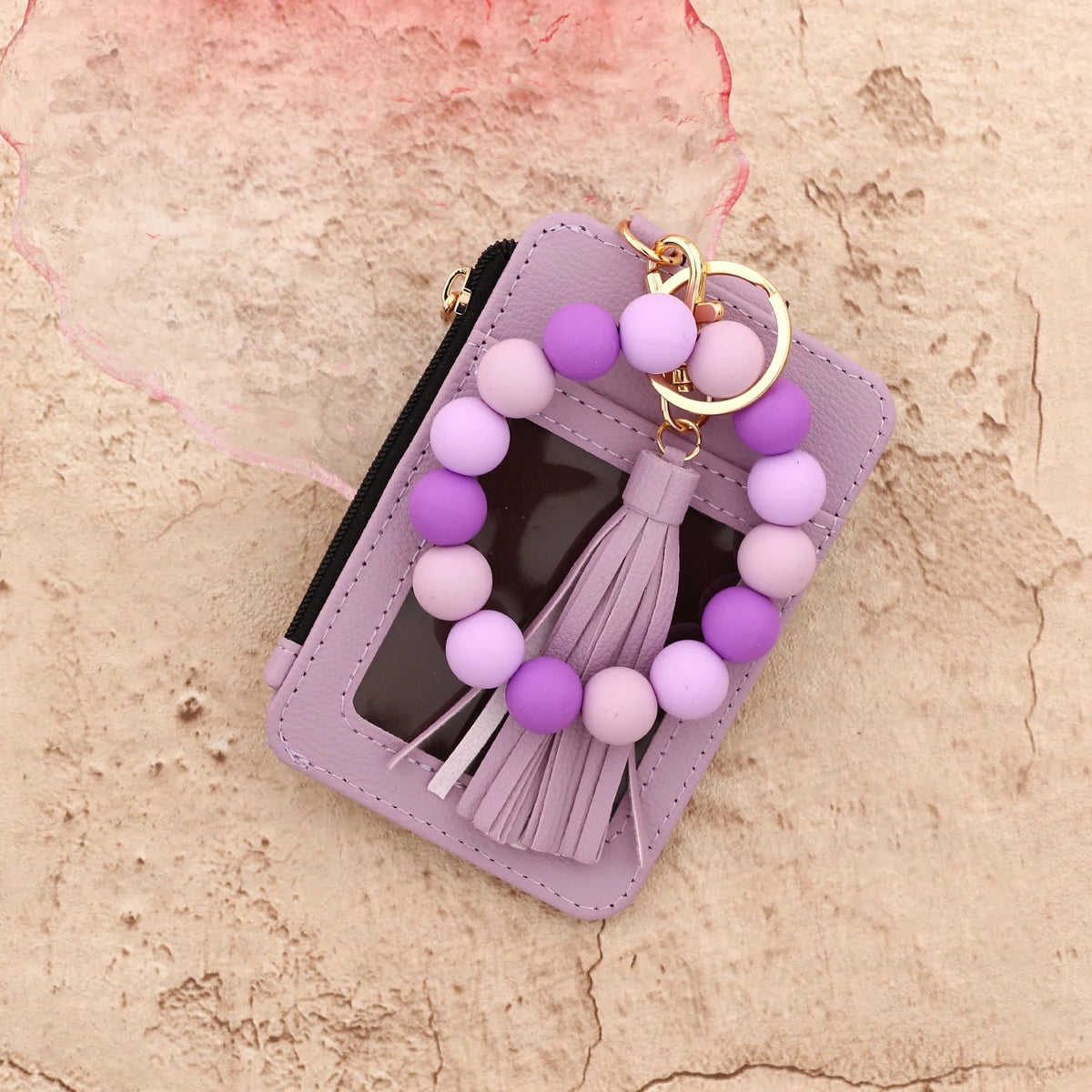 A purple beaded bracelet is displayed inside a lavender leather card holder with a gold keychain.