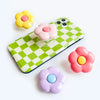 A colorful foldable phone grip ring stand featuring pink, yellow, and purple flower shapes.