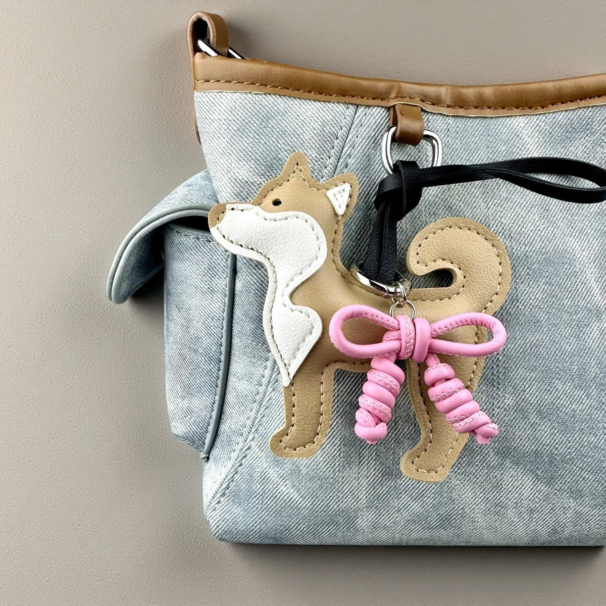 Bolsa de mezclilla azul claro con un dije de perro Shiba Inu color canela y un lazo de cuero trenzado rosa.