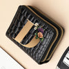 A black PU leather double-zip clutch wallet with gold trim and a floral accent resting on a beige surface.