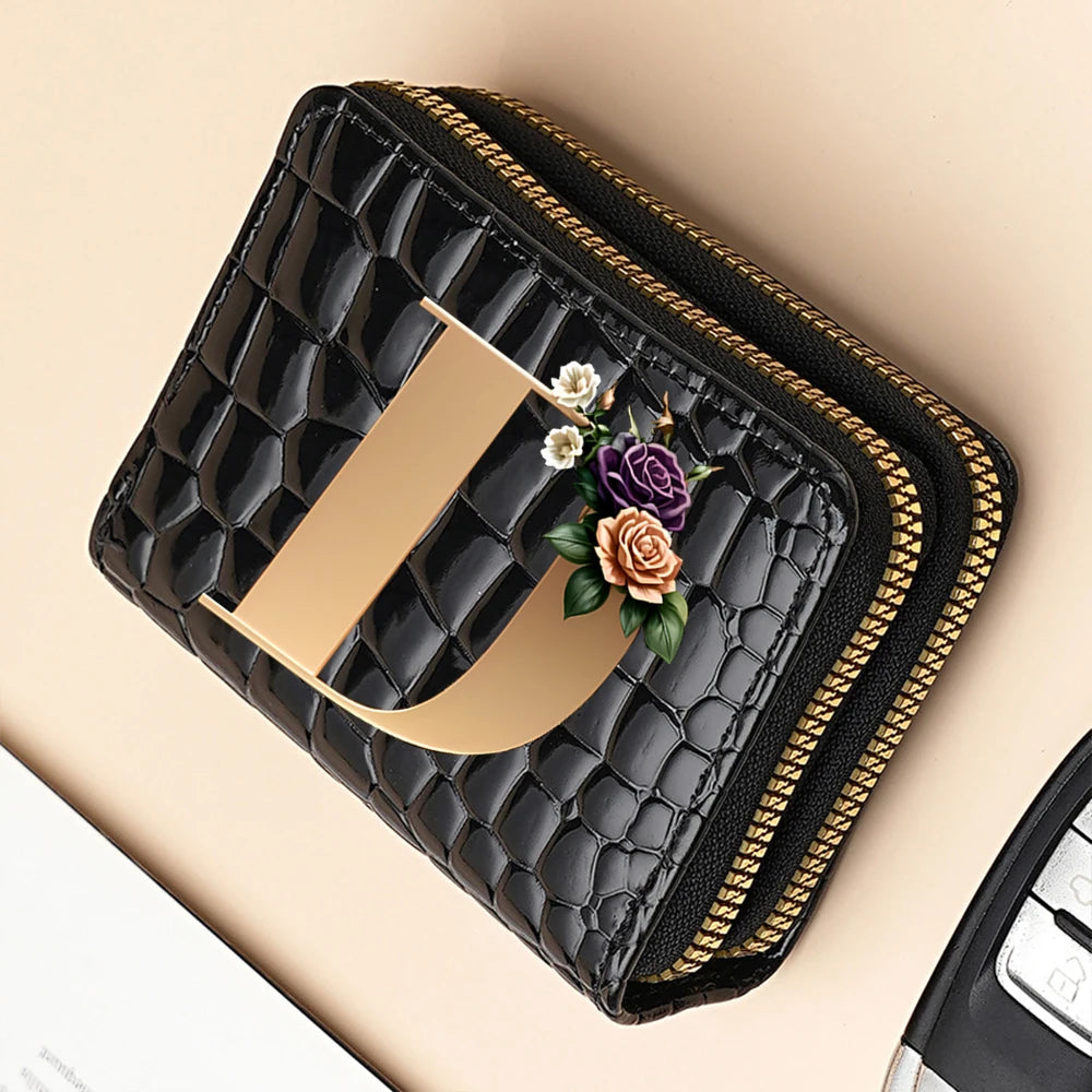 A black PU leather double-zip clutch wallet with gold trim and a floral accent resting on a beige surface.