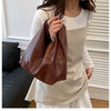 A woman holds a brown leather minimalist crossbody tote bag while wearing a cream-colored top.