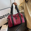 A pink leather travel tote bag with black straps resting on a dark surface next to a light-colored coat.