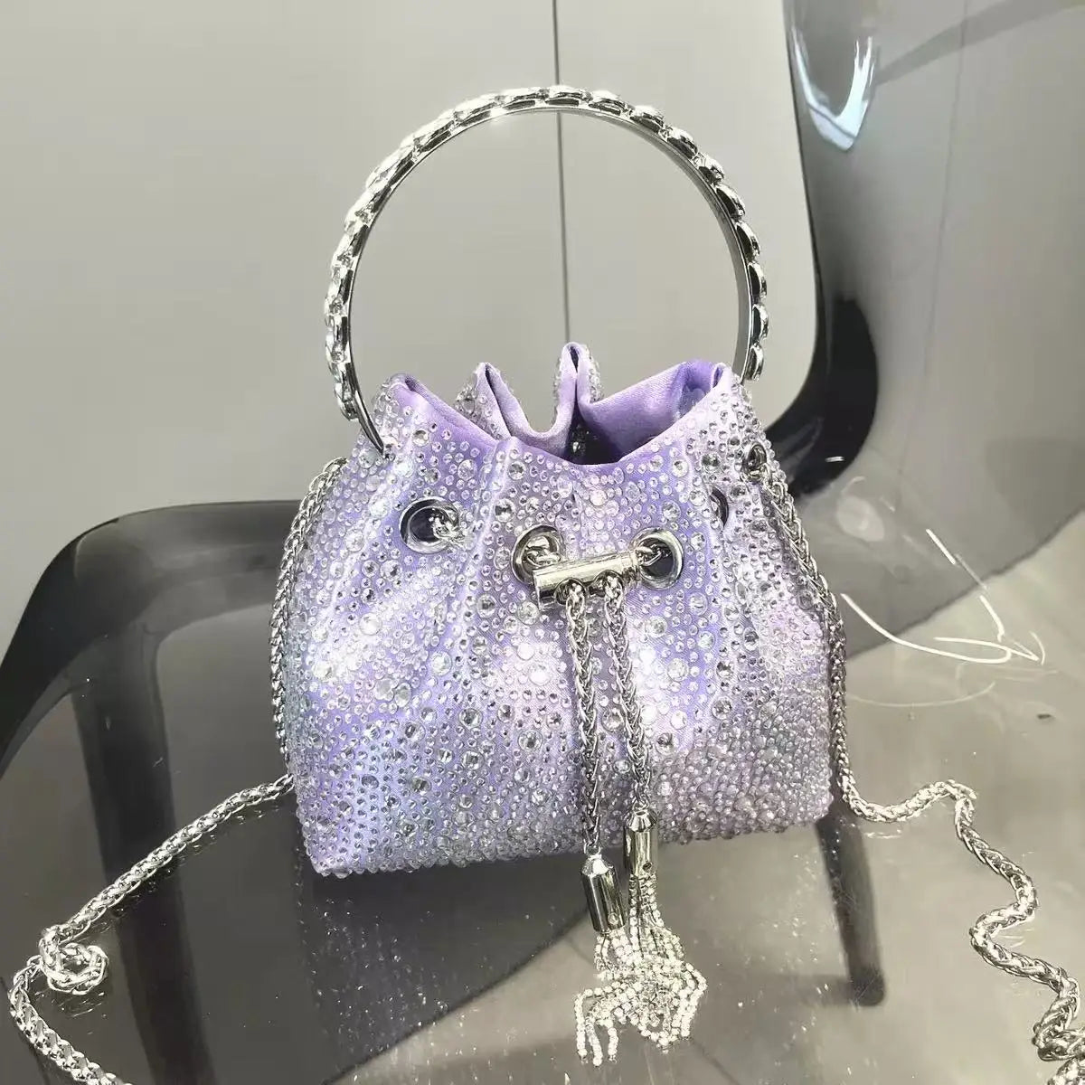 A purple crystal-embellished evening clutch with a silver chain strap displayed on a black surface.