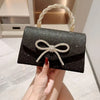 Clutch de noche con lazo brillante negro y asa de cuentas doradas, sostenido por una mano.