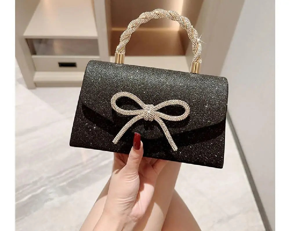 Clutch de noche con lazo brillante negro y asa de cuentas doradas, sostenido por una mano.