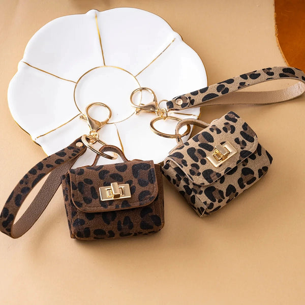 A leopard print faux leather keychain bag with gold hardware rests on a white tile background.