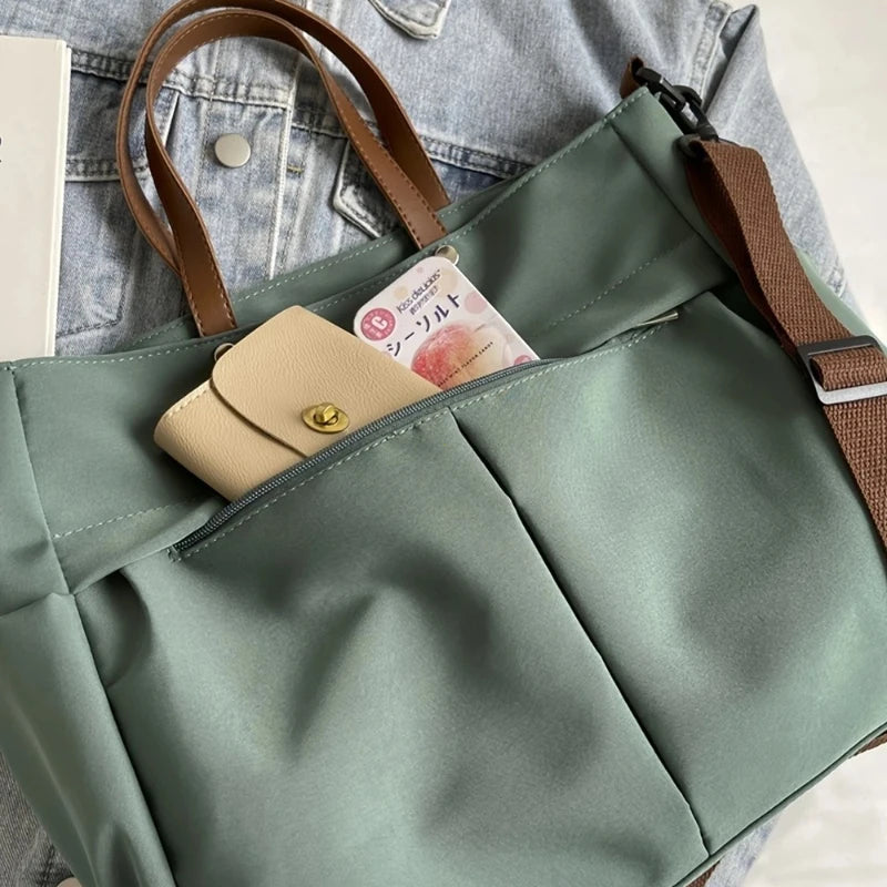 A light sage green nylon tote bag with brown leather straps and a flap pocket featuring a small tag.