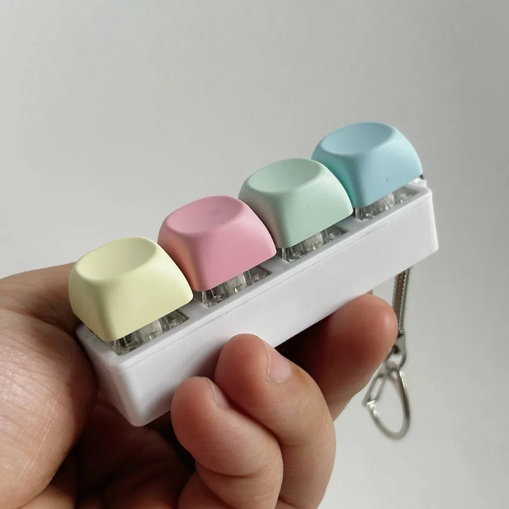 A hand holds a white tactile stress relief keyboard fidget toy with five pastel-colored buttons.