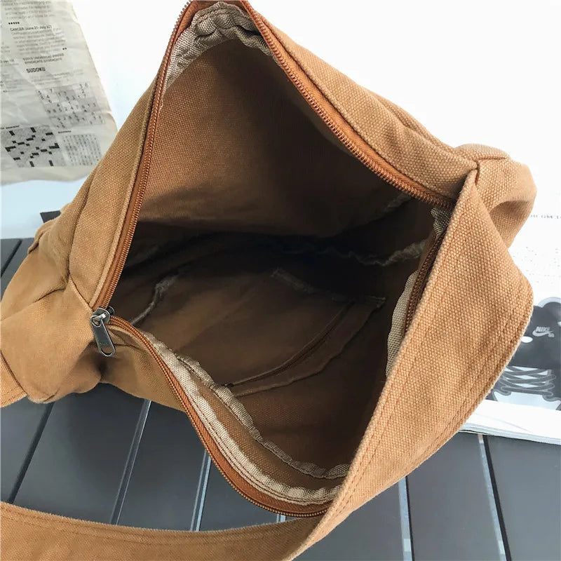 A brown canvas crossbody shoulder bag is shown open, revealing the interior lining and stitching.
