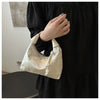 A close-up shot of a cream embroidered crossbody shoulder bag held by a person wearing a black dress.