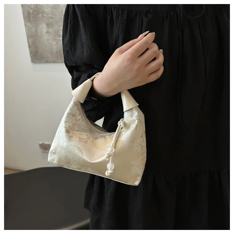 A close-up shot of a cream embroidered crossbody shoulder bag held by a person wearing a black dress.