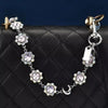 A delicate silver chain necklace featuring crystal petals and a crescent moon charm on a black quilted bag.