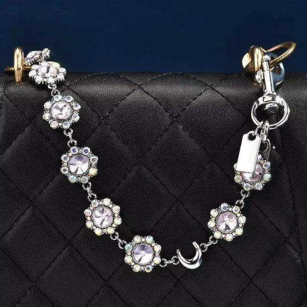 A delicate silver chain necklace featuring crystal petals and a crescent moon charm on a black quilted bag.