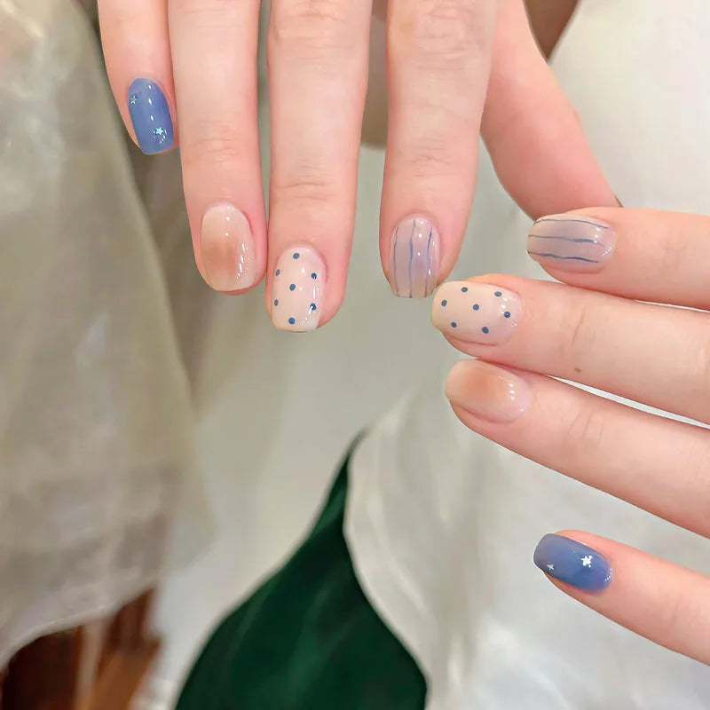A hand displays a set of cute cartoon press-on nails in various shades of blue and white with small star accents.