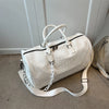 A white crocodile grain PU leather travel duffle bag with light beige straps resting on a carpet.