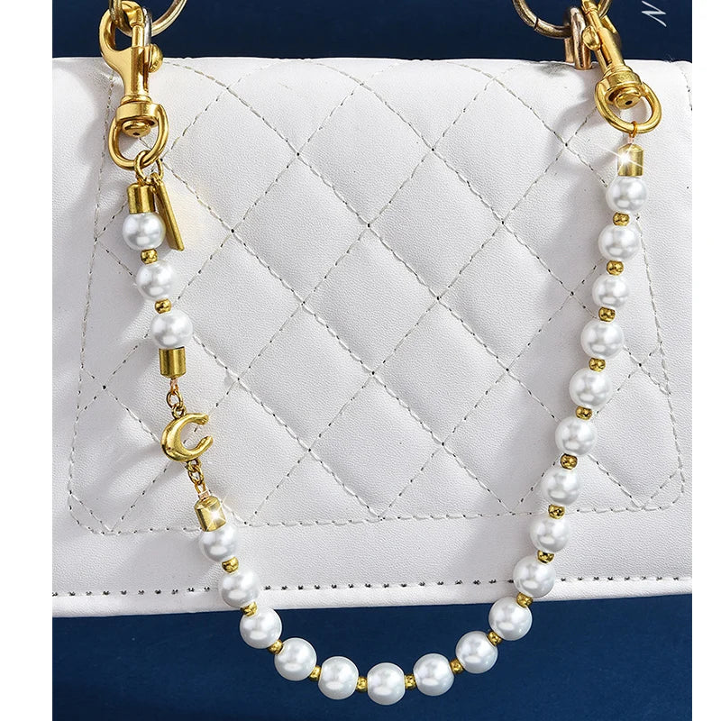 A pearl and gold letter charm necklace displayed against a white quilted leather bag.