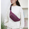 A woman is wearing a purple quilted nylon crossbody belt bag on her white sweatshirt.