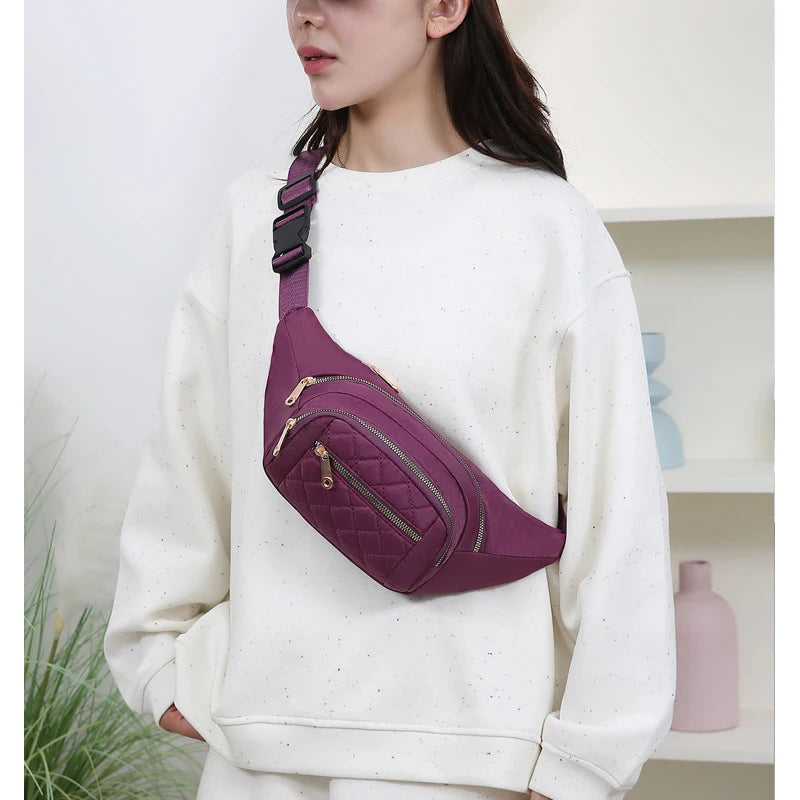 A woman is wearing a purple quilted nylon crossbody belt bag on her white sweatshirt.