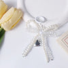 A clear pearl keychain with a bow design and a silver heart charm resting on a white surface next to a yellow tulip.