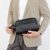 A man holds a black vintage PU leather clutch bag against a light beige blazer.