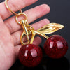 A gold-colored keychain featuring a stylized cherry fruit charm and a red glittery spherical bead.