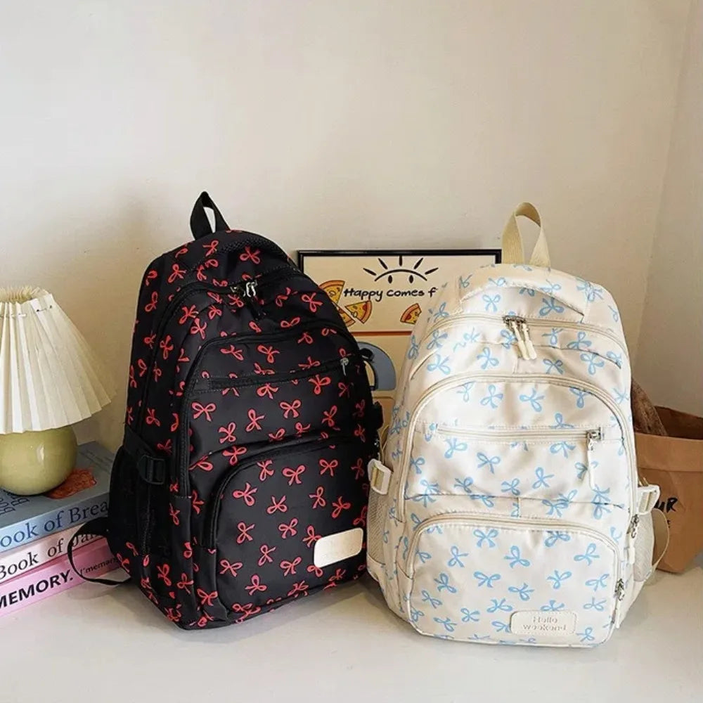A pair of cute bow print nylon travel backpacks, one black and one white, are displayed on a white surface.