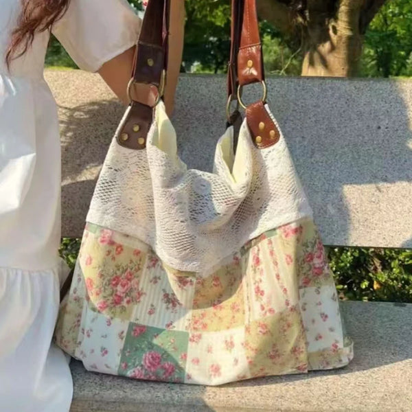 A light-colored patchwork shoulder bag with floral patterns is being held by a person outdoors.