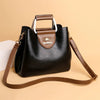 Sac bandoulière vintage en cuir noir avec doublure et sangle marron, posé sur une surface beige.