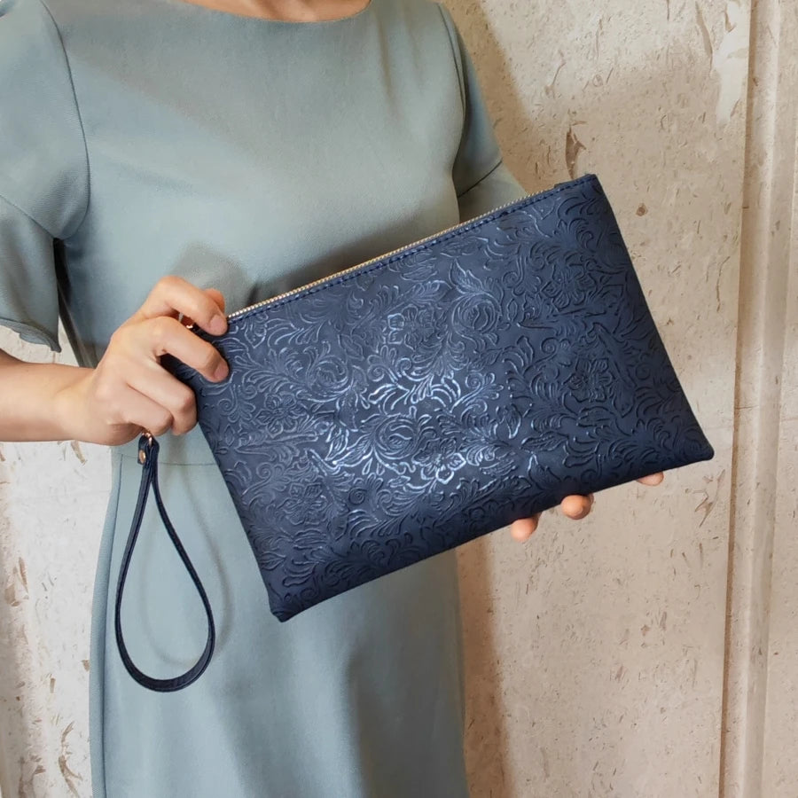 Una mano sostiene un bolso de cuero PU con estampado floral azul oscuro contra un vestido verde claro.