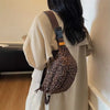 A woman is holding a leopard print crossbody bag with a brown adjustable strap against a light beige garment.
