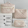 A set of three floral print quilted cosmetic bags in beige and pink tones displayed on a white shelf.