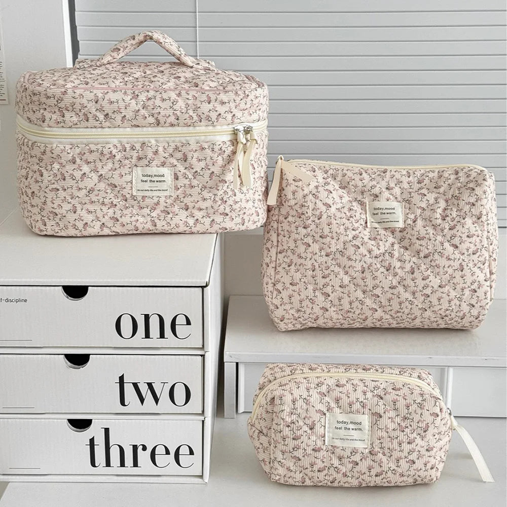 A set of three floral print quilted cosmetic bags in beige and pink tones displayed on a white shelf.
