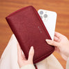 A hand holds a maroon PU leather wallet with a zipper closure, demonstrating RFID protection.
