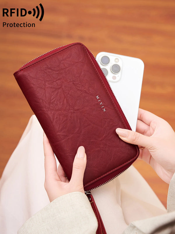 A hand holds a maroon PU leather wallet with a zipper closure, demonstrating RFID protection.