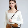 A model wearing a cream long-sleeved top and brown skirt, carrying a black leather mini shoulder bag.