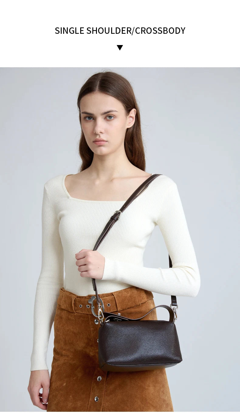 A model wearing a cream long-sleeved top and brown skirt, carrying a black leather mini shoulder bag.