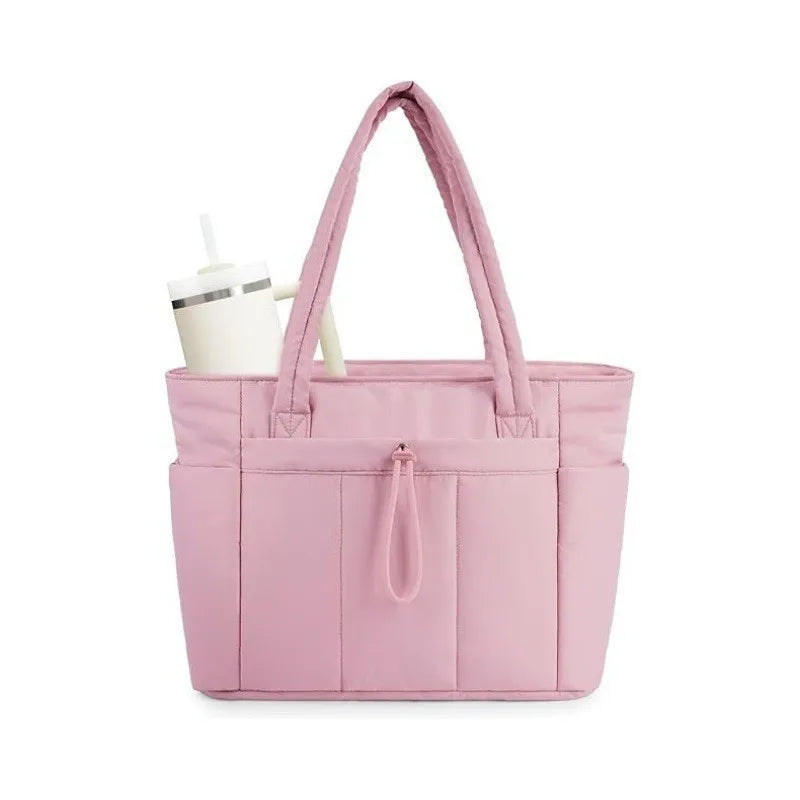 A light pink quilted tote bag with a canvas strap and a white cup resting beside it.