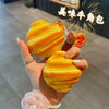 A hand holds a bright yellow silicone protective case for wireless earbuds against a dark background.