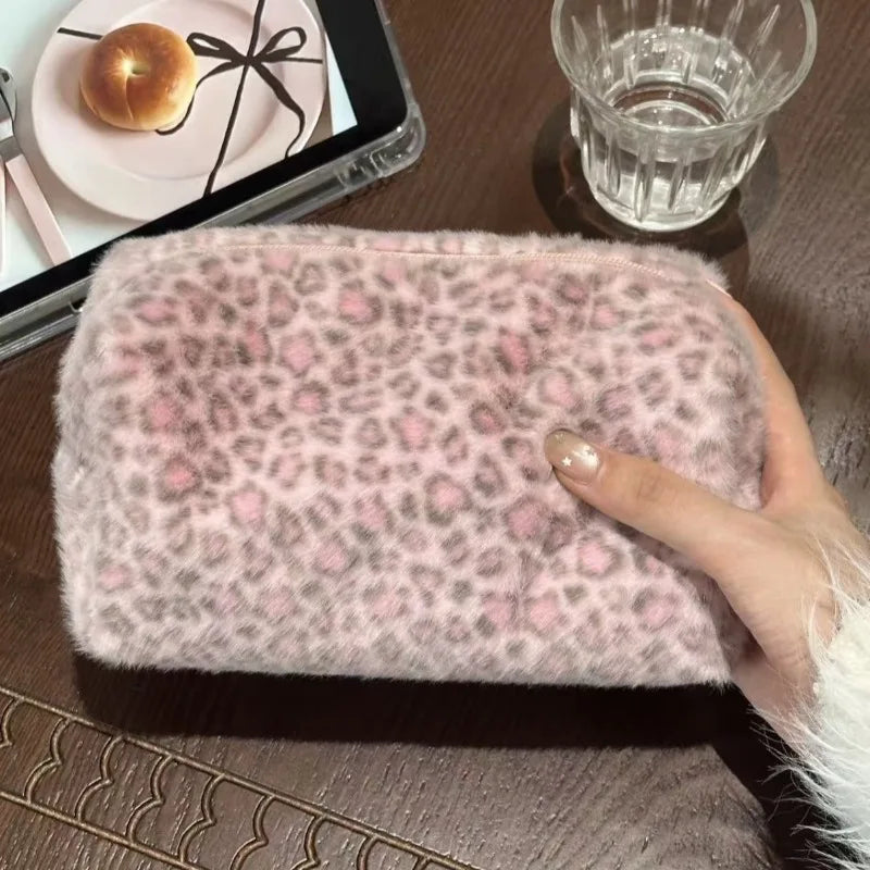Una mano sostiene una bolsa de maquillaje para viajar con estampado de leopardo rosa sobre una superficie de madera junto a u