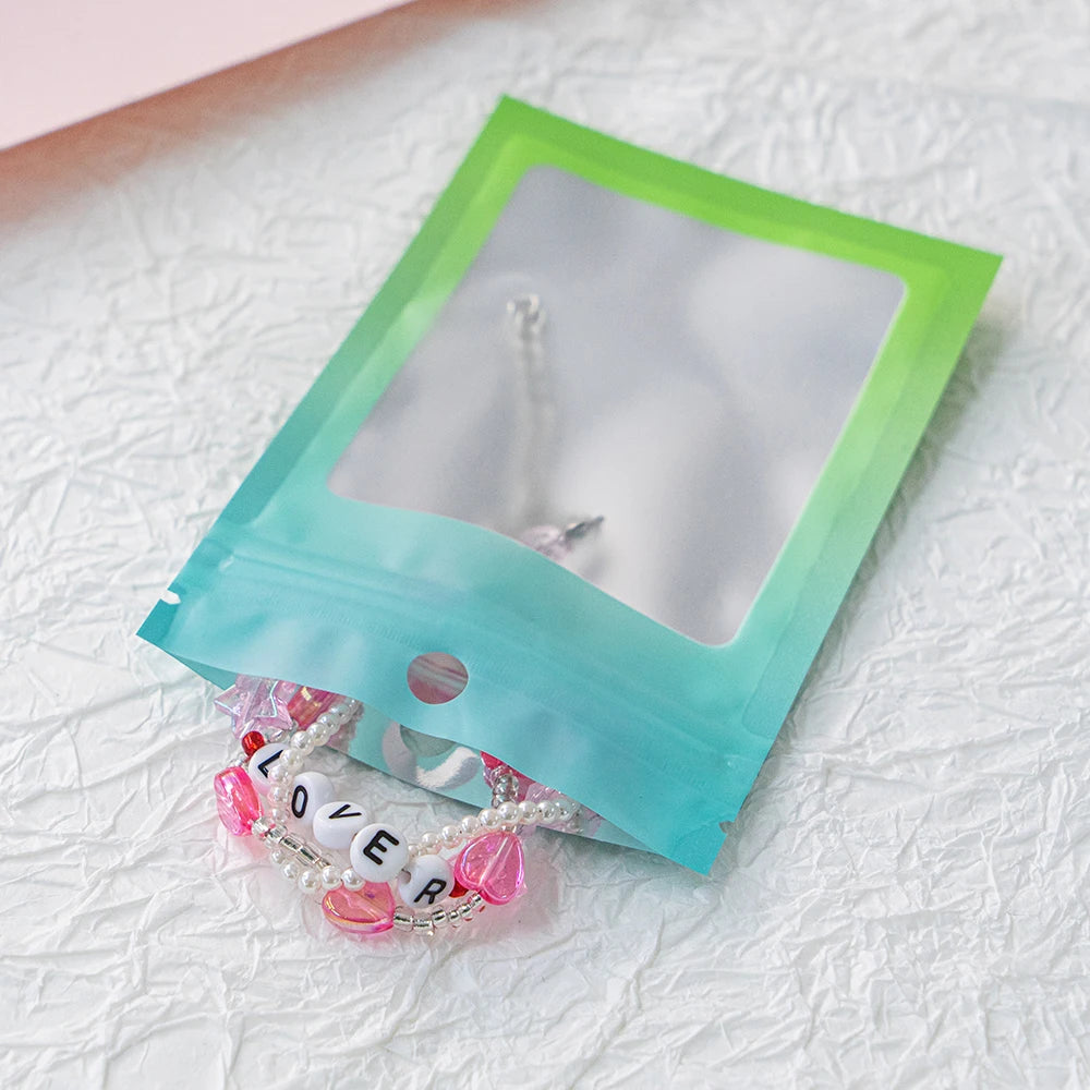 A clear plastic bag with a gradient color design holds a delicate pearl and pink bead necklace.