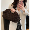 A woman holds a dark brown straw woven tote handbag against a white blazer and a patterned skirt.
