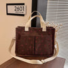 A dark brown canvas tote bag with a pink strawberry pattern resting on a wooden surface.