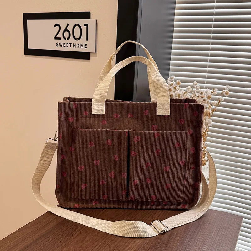 A dark brown canvas tote bag with a pink strawberry pattern resting on a wooden surface.