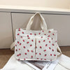 A white canvas tote bag with a red strawberry pattern, shown against a light gray background.