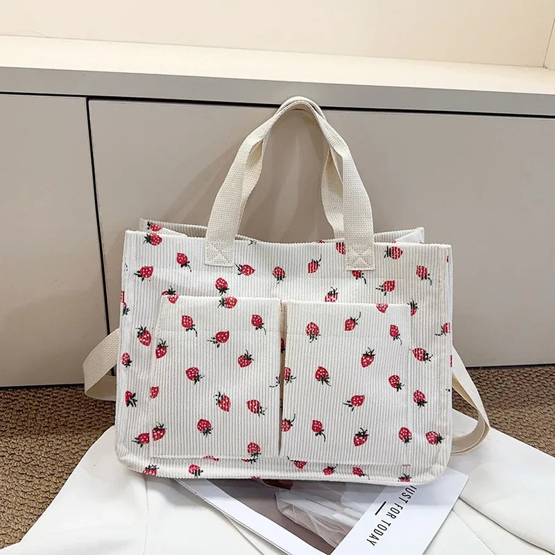 A white canvas tote bag with a red strawberry pattern, shown against a light gray background.