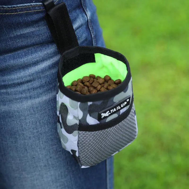 A black pet training treat pouch with a mesh pocket filled with brown dog treats, worn on a person's jeans.