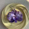A purple orchid flower keychain is displayed on a light yellow plate.