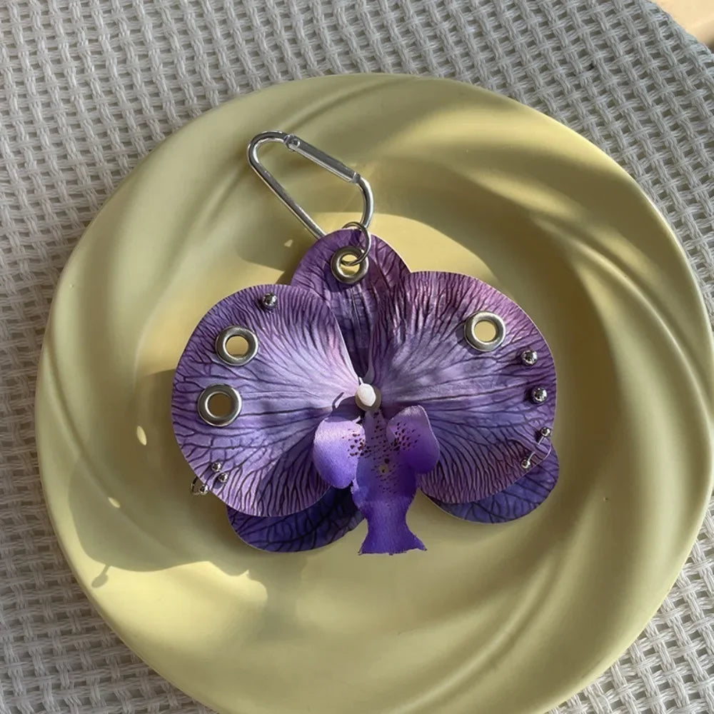 A purple orchid flower keychain is displayed on a light yellow plate.