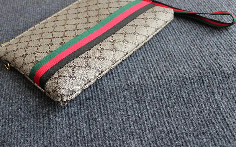Beige gemusterte Clutch-Tasche mit roten und schwarzen Streifen liegt auf einer grauen Stoffoberfläche.